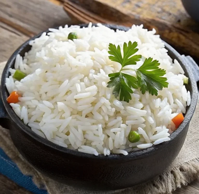 Steam cooked rice recipe is served in a black decorative bowl on a wooden table, garnished with a sprig of fresh parsley and topped with small pieces of carrots and green peas.
