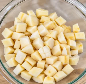 A clear glass bowl is filled to the brim with peeled and uniformly diced raw potatoes. These little cubes are prepped