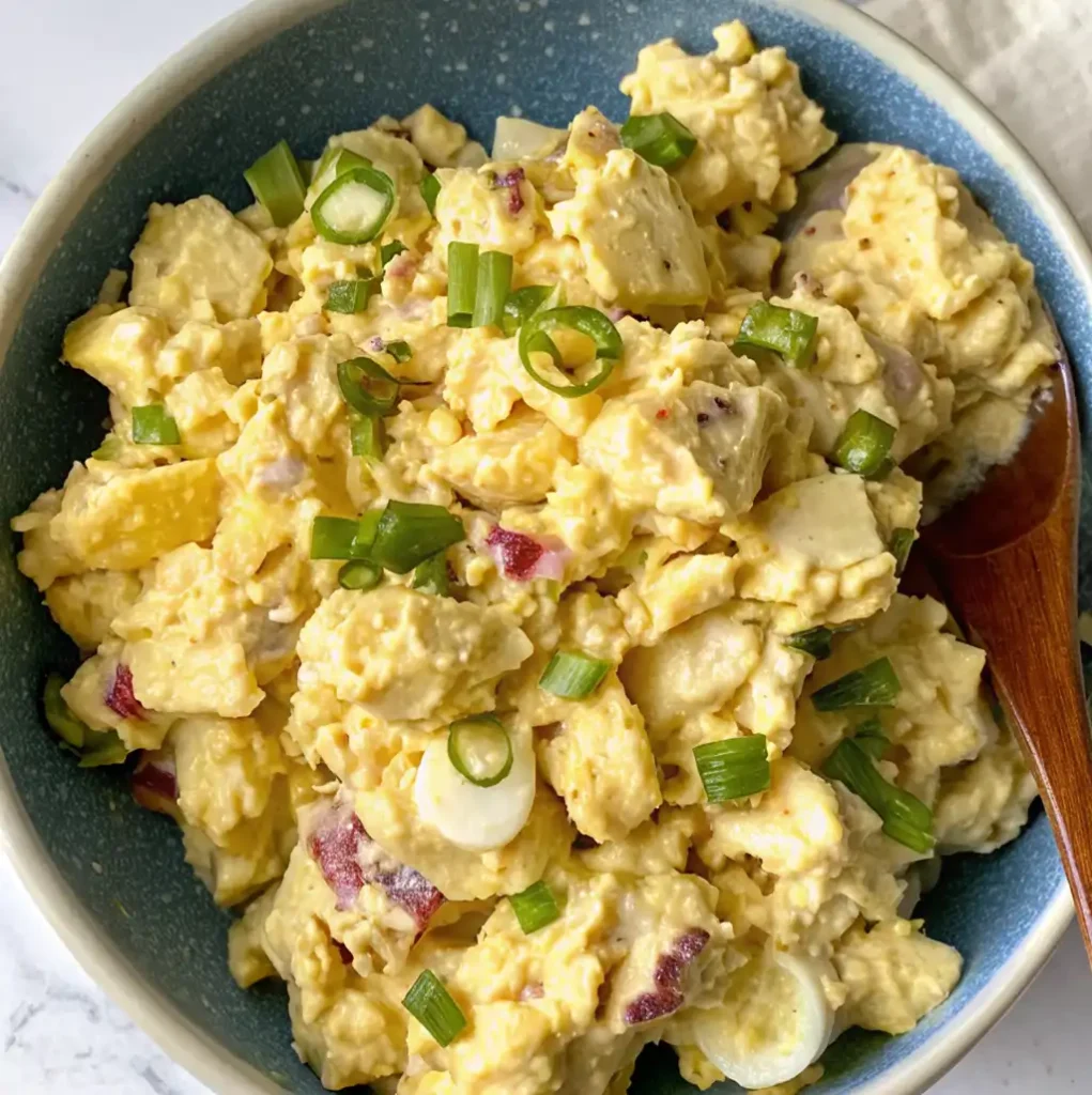 Creamy potato salad with boiled eggs served in a blue bowl, garnished with plenty of chopped green onions. The potatoes and eggs are covered with sauce.