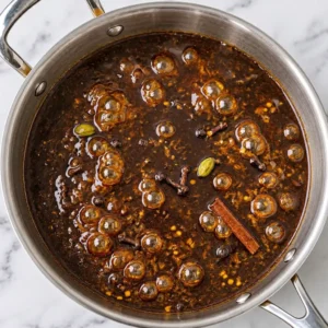 Homemade Worcestershire sauce simmering in a stainless steel pot with whole spices, cinnamon sticks, cloves, and cardamom pods.