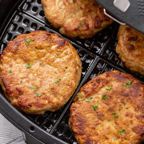 frozen turkey burger air fryer. Four juicy, golden-brown turkey burger patties seasoned with fresh herbs sit inside a black air fryer basket, perfectly cooked with a crisp exterior and tender, flavorful center.