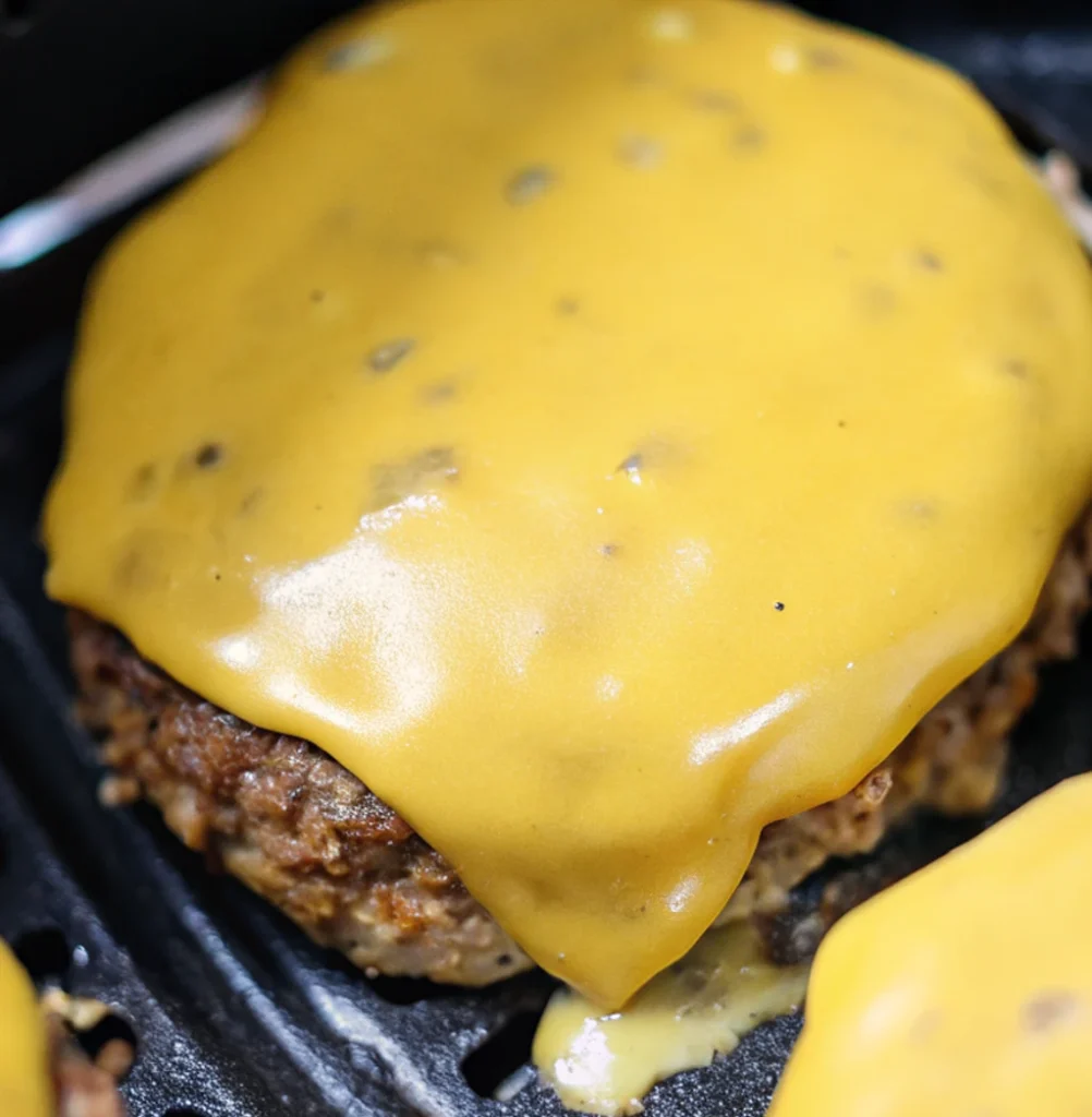 A thick, juicy turkey burger patty topped with a perfectly melted, smooth layer of yellow cheddar cheese, cooked to a golden brown inside a dark air fryer basket.