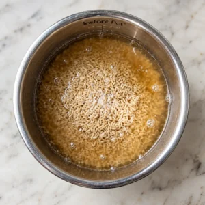 Top view of the Instant Pot's steel inner pot containing uncooked brown rice submerged in cooking liquid with air bubbles.