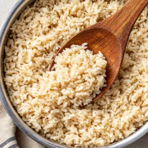 A close-up view of cooked, fluffy brown rice instant pot, with a wooden spoon stirring the grains.
