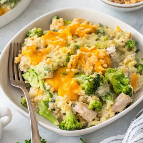 easy chicken broccoli rice casserole in a white bowl. The dish features tender chicken chunks, bright green broccoli florets, and creamy rice topped with melted cheddar.
