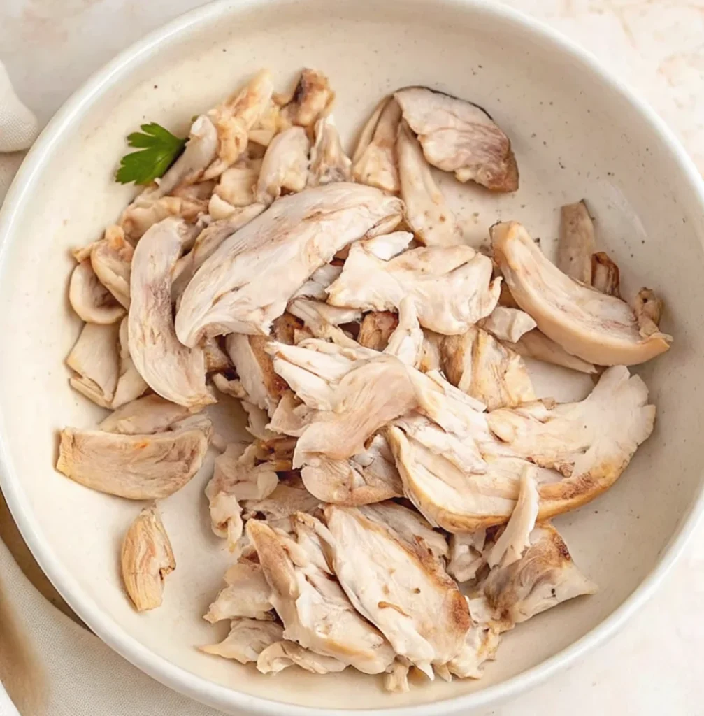 Cooked, shredded pieces of tender chicken breast and thigh meat piled in a light-colored ceramic bowl, prepared as a hearty protein base for a traditional Hawaiian long rice recipe.