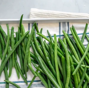 fresh, vibrant green beans scattered across a white and blue striped kitchen towel on a tray, highlighting their slender shape and crisp, bright green texture.
