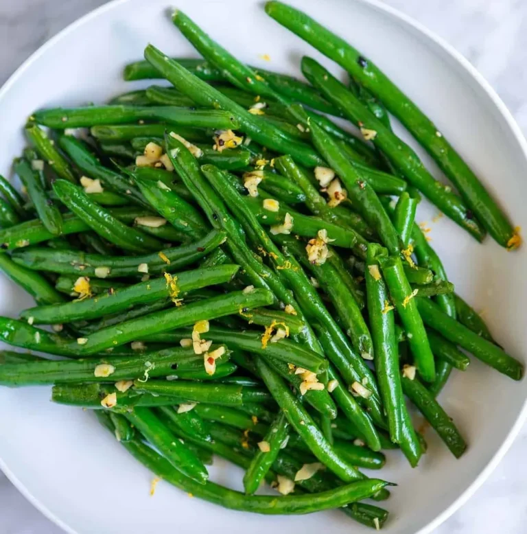 A finished dish of bright french green beans served in a white bowl, garnished with minced garlic and fresh lemon zest for a flavorful, vibrant side dish.