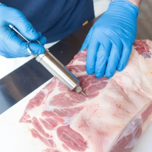 for Award Winning Brisket Injection Recipe A person wearing blue nitrile gloves uses a professional stainless steel meat injector to inject a smoking solution into a raw meat breast.