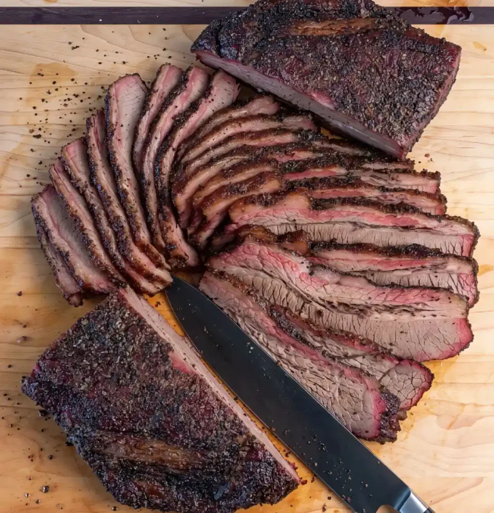How to Cook Beef Brisket: An overhead view of a sliced brisket arranged on a wooden board with a large knife, highlighting the uniform slices and dark, seasoned bark.