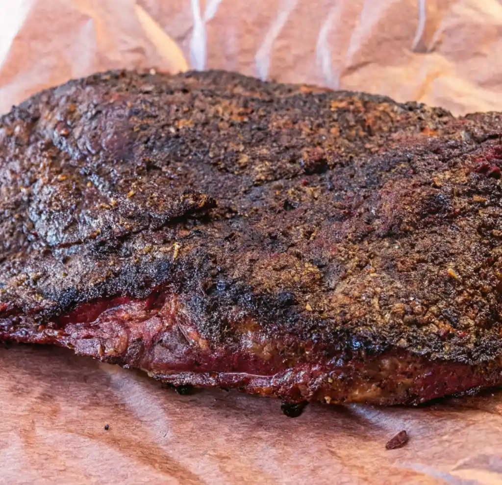 A whole piece of smoked beef brisket with a dark, crispy crust, placed on brown butcher paper, ready for packaging.