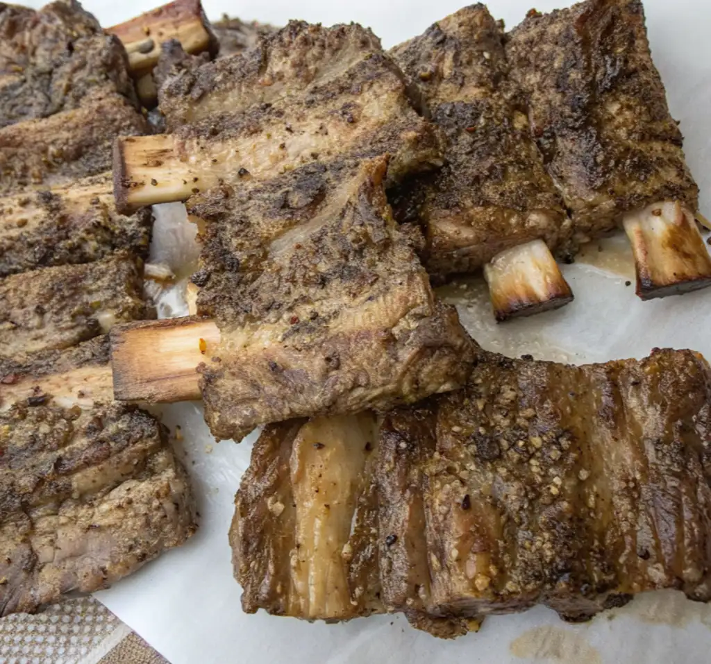 Beef short ribs appear pale and tender after being removed from the sous-vide bag, resting on parchment paper with visible seasoning and rendered fat before the final searing process.