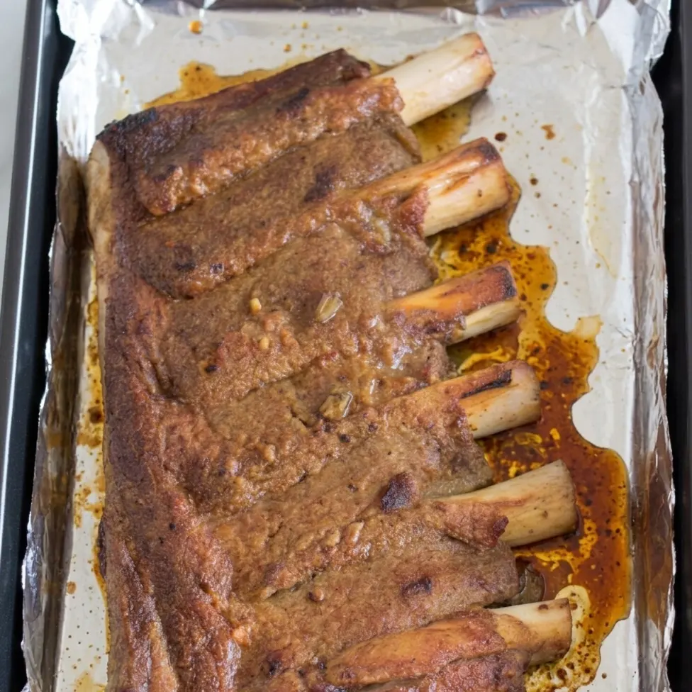 Cooked beef ribs resting on a foil-lined baking sheet, showing a caramelized brown crust and rendered juices. The tender meat is pulled back from the bones after beef ribs in oven at 350.