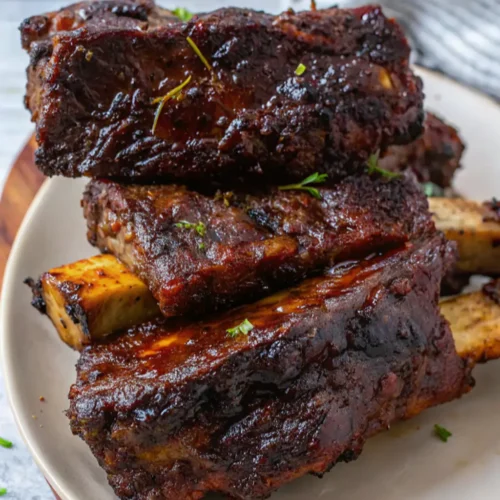 Tender, slow-cooked beef short ribs featuring a rich, In the style how to cook beef ribs dark sear and savory glaze. Served in a shallow bowl with natural juices and garnished with a sprinkle of fresh green herbs.