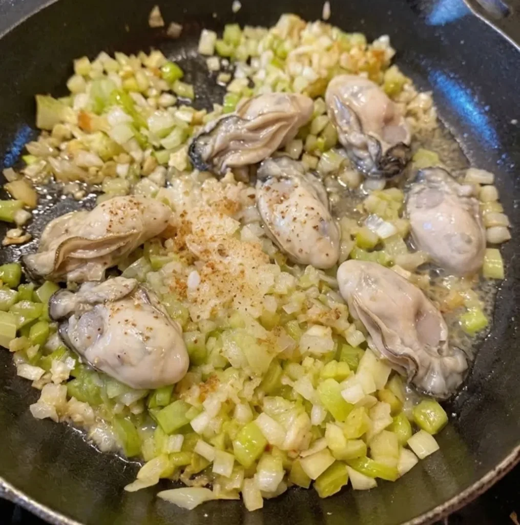 Sautéed oysters and diced vegetables cooking together in a cast iron skillet. This process shot captures the aromatic base for a traditional seafood oyster dressing recipe.