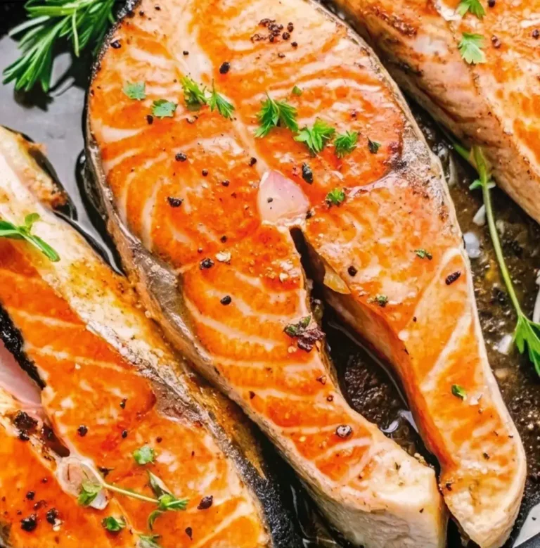 Pan-fried salmon fillets, with a golden-brown crust, seasoned with ground black pepper and fresh herbs, and left in a cast-iron skillet to achieve a tender texture—how to cook salmon