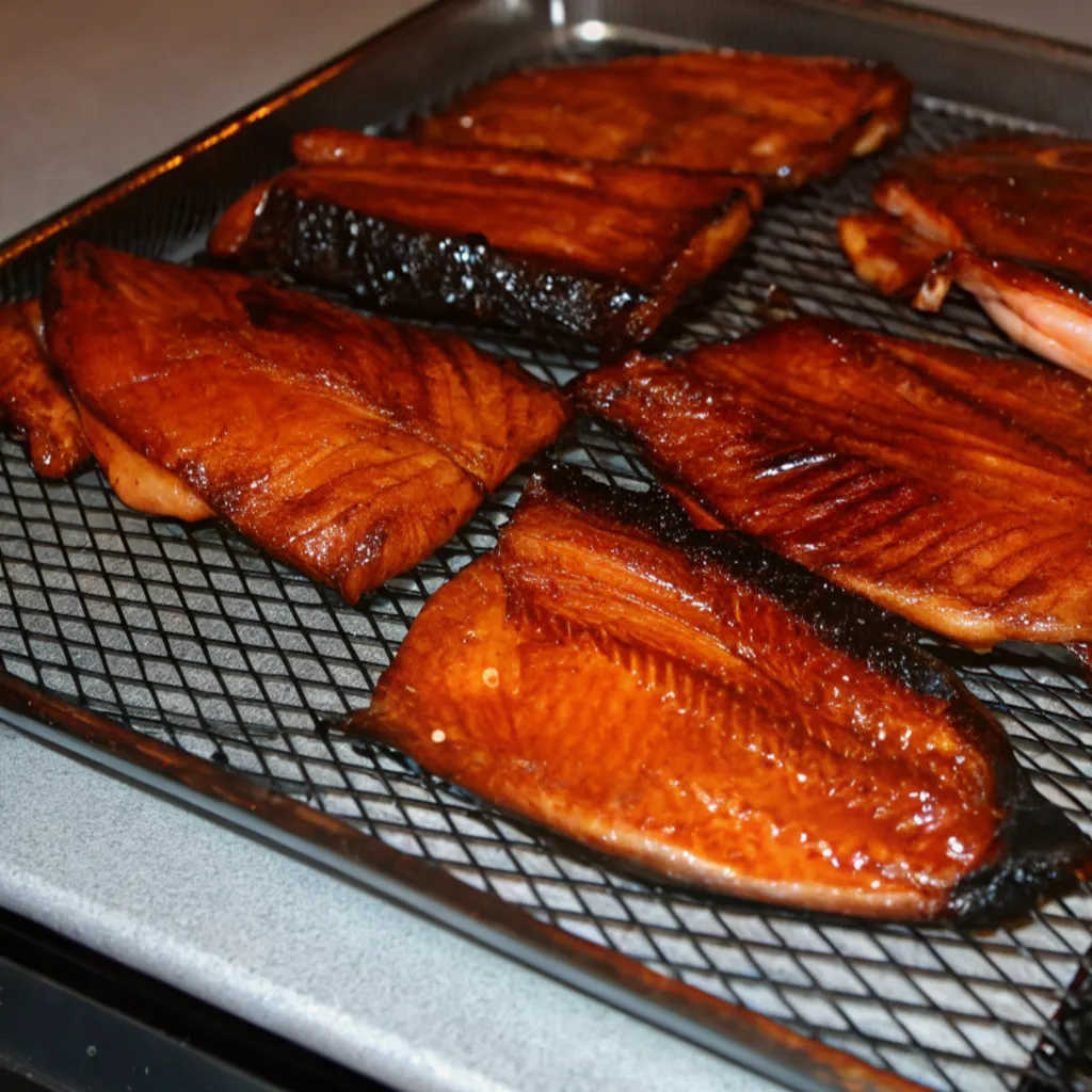 Dark amber-colored slices of smoked salmon, covered in a thick layer of smoke, arranged on a wire cooling rack.