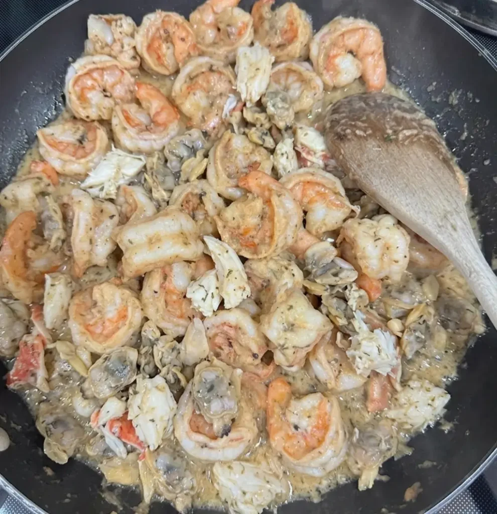 A skillet filled with sautéed shrimp, crab meat, and oysters simmering in a seasoned butter sauce, being prepared as the flavorful seafood base for a traditional Thanksgiving dressing or stuffing.