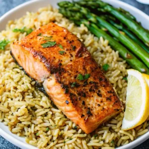 A perfectly Broiled Salmon Recipe fillet seasoned with herbs, served over a bed of fluffy seasoned rice with a side of tender green asparagus and a fresh lemon wedge.