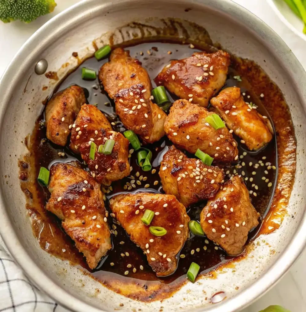 Grilled teriyaki chicken pieces, coated with teriyaki sauce, sesame seeds and sliced spring onions, in a metal pan. It gives Panda Express's grilled teriyaki chicken the perfect flavour.