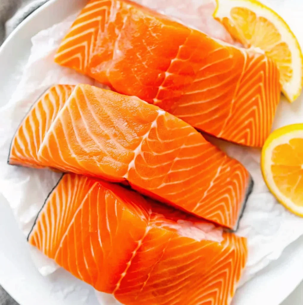 Three vibrant, raw salmon fillets with beautiful white marbling rest on white parchment paper.