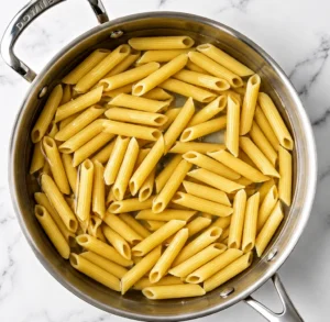 Penne pasta boiling in a large stainless steel pot of water on a marble countertop
