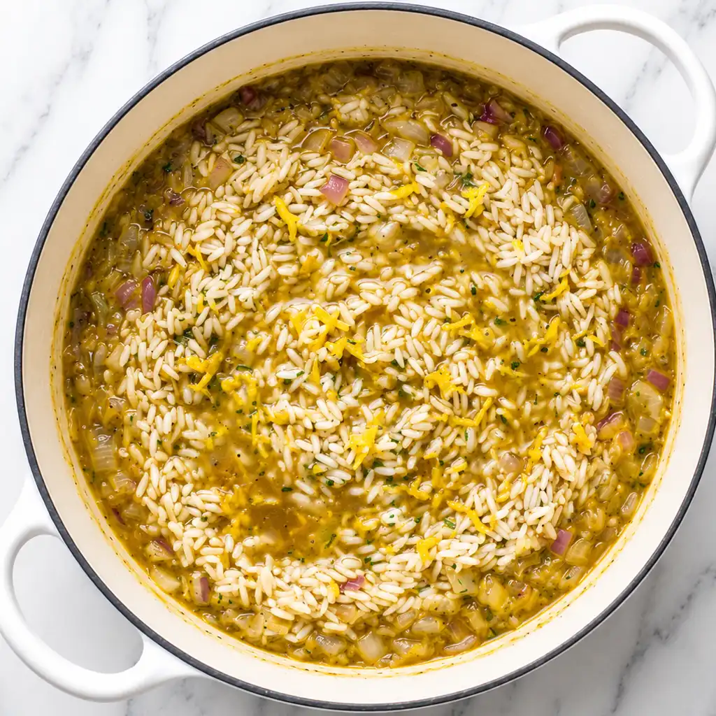 Overhead shot of flavorful orange rice mixed with chopped red onions and fresh citrus zest simmering inside a large white pot, capturing a fresh, home-cooked culinary meal.