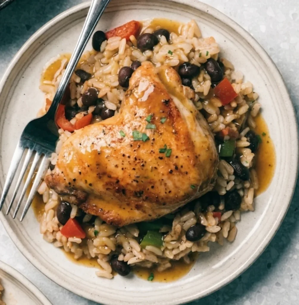 chicken rice and beans plated featuring a tender roasted chicken thigh topped with fresh herbs, paired with flavorful white rice, black beans, and savory sauce.