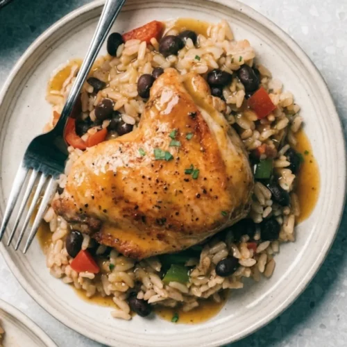 chicken rice and beans plated featuring a tender roasted chicken thigh topped with fresh herbs, paired with flavorful white rice, black beans, and savory sauce.