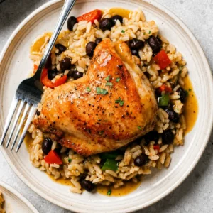 chicken rice and beans plated featuring a tender roasted chicken thigh topped with fresh herbs, paired with flavorful white rice, black beans, and savory sauce.
