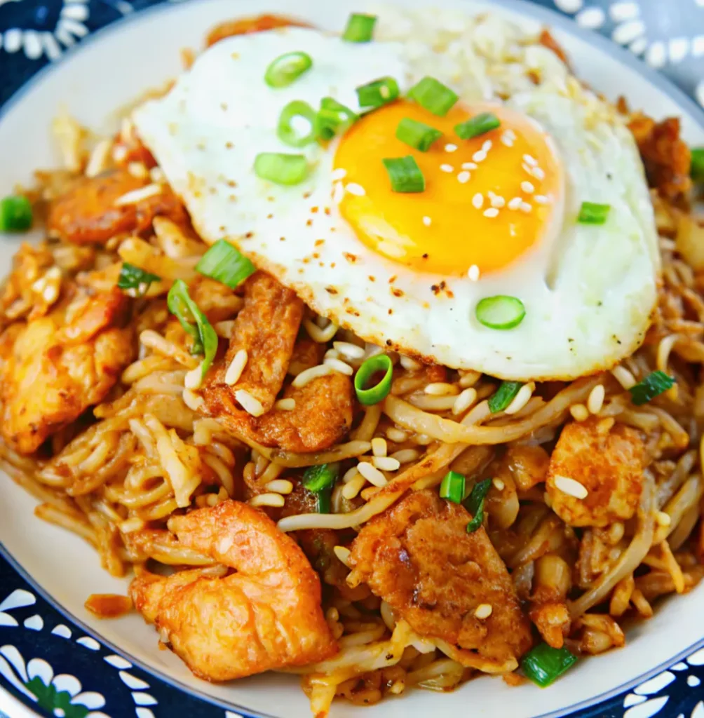 a plate of savory Kimchi Chicken Fried Rice is garnished with sesame seeds, green onions, and a sunny-side-up fried egg.