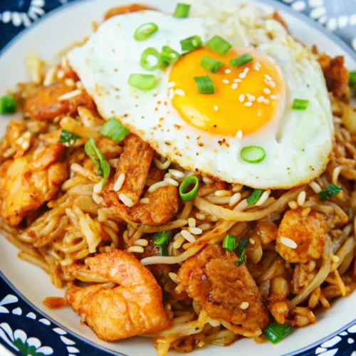 a plate of savory Kimchi Chicken Fried Rice is garnished with sesame seeds, green onions, and a sunny-side-up fried egg.