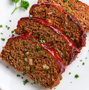 Slices of juicy, cooked Air Fryer Meatloaf Recipe featuring a glossy, caramelized red glaze and visible onion bits, served on a white platter garnished with fresh chopped parsley.