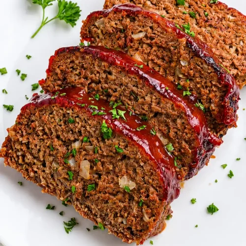 Slices of juicy, cooked Air Fryer Meatloaf Recipe featuring a glossy, caramelized red glaze and visible onion bits, served on a white platter garnished with fresh chopped parsley.