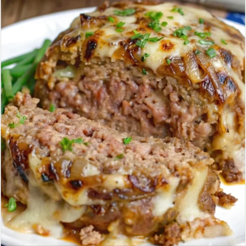 A sliced French Onion Meatloaf Recipe topped with melted Gruyere cheese, caramelized onions, served on a white plate