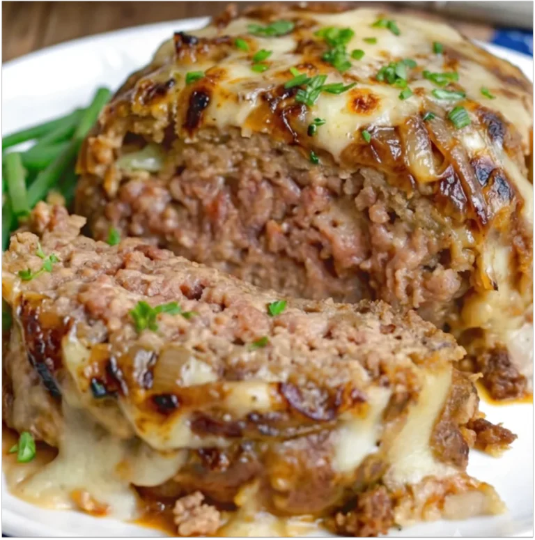 A sliced French Onion Meatloaf Recipe topped with melted Gruyere cheese, caramelized onions, served on a white plate